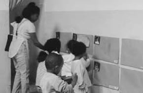 As crianças da creche Casa da Criança fixam os trabalhos sobre suas pastas, penduradas na parede, identificadas com fotos.